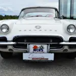 Weiße Corvette C1 Roadster 327 Dual Top, Baujahr 1962, von vorne aufgenommen, mit sichtbarem Emblem und Hardtop.