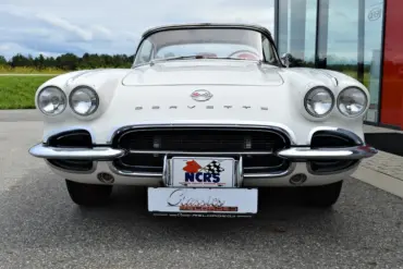 Weiße Corvette C1 Roadster 327 Dual Top, Baujahr 1962, von vorne aufgenommen, mit sichtbarem Emblem und Hardtop.