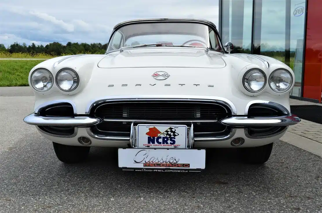 Weiße Corvette C1 Roadster 327 Dual Top, Baujahr 1962, von vorne aufgenommen, mit sichtbarem Emblem und Hardtop.