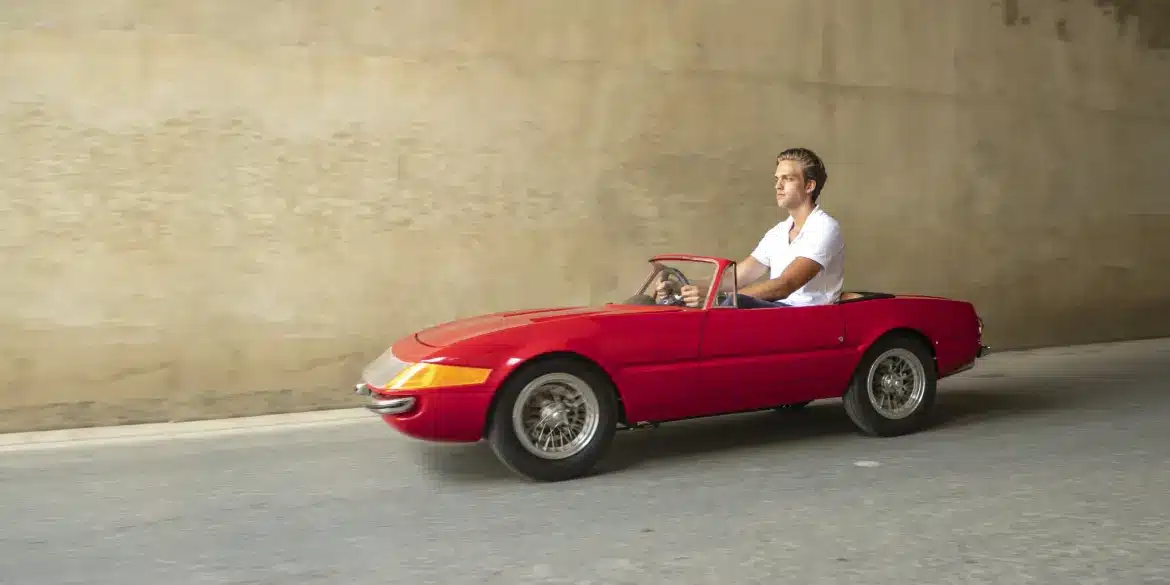 Ein Mann fährt ein rotes, maßstabsgetreues Junior-Car-Modell Daytona, das optisch klassischen Sportwagen nachempfunden ist.