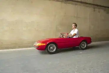 Ein Mann fährt ein rotes, maßstabsgetreues Junior-Car-Modell Daytona, das optisch klassischen Sportwagen nachempfunden ist.