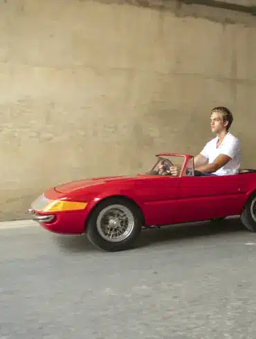 Ein Mann fährt ein rotes, maßstabsgetreues Junior-Car-Modell Daytona, das optisch klassischen Sportwagen nachempfunden ist.