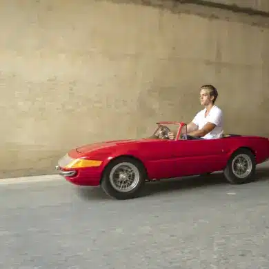 Ein Mann fährt ein rotes, maßstabsgetreues Junior-Car-Modell Daytona, das optisch klassischen Sportwagen nachempfunden ist.