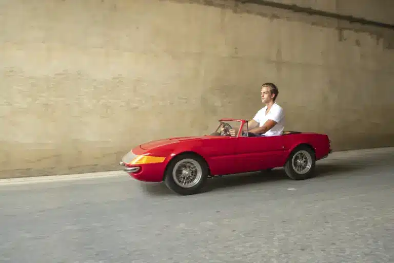 Ein Mann fährt ein rotes, maßstabsgetreues Junior-Car-Modell Daytona, das optisch klassischen Sportwagen nachempfunden ist.