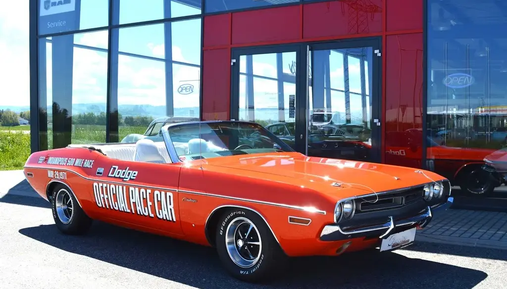 Dodge Challenger Convertible Pace Car von 1971 in Hemi Orange mit offizieller Pace Car Beschriftung, vor einem Showroom geparkt.