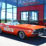 Dodge Challenger Convertible Pace Car von 1971 in Hemi Orange mit offizieller Pace Car Beschriftung, vor einem Showroom geparkt.