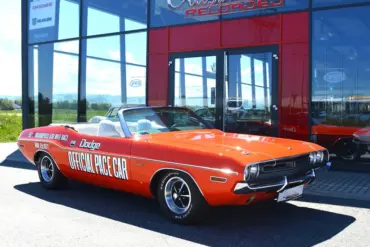 Dodge Challenger Convertible Pace Car von 1971 in Hemi Orange mit offizieller Pace Car Beschriftung, vor einem Showroom geparkt.