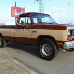 Dodge D150 Ram Frame-Off von 1984 in Western Brown Metallic und Creme, Seitenansicht auf Parkplatz.