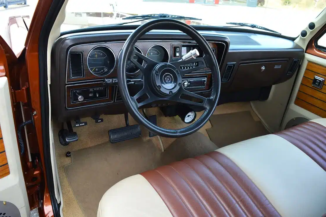 Restaurierter Innenraum eines Dodge D150 Ram von 1984 mit braun-beigen Sitzen, Holzapplikationen und originalgetreuem Armaturenbrett.