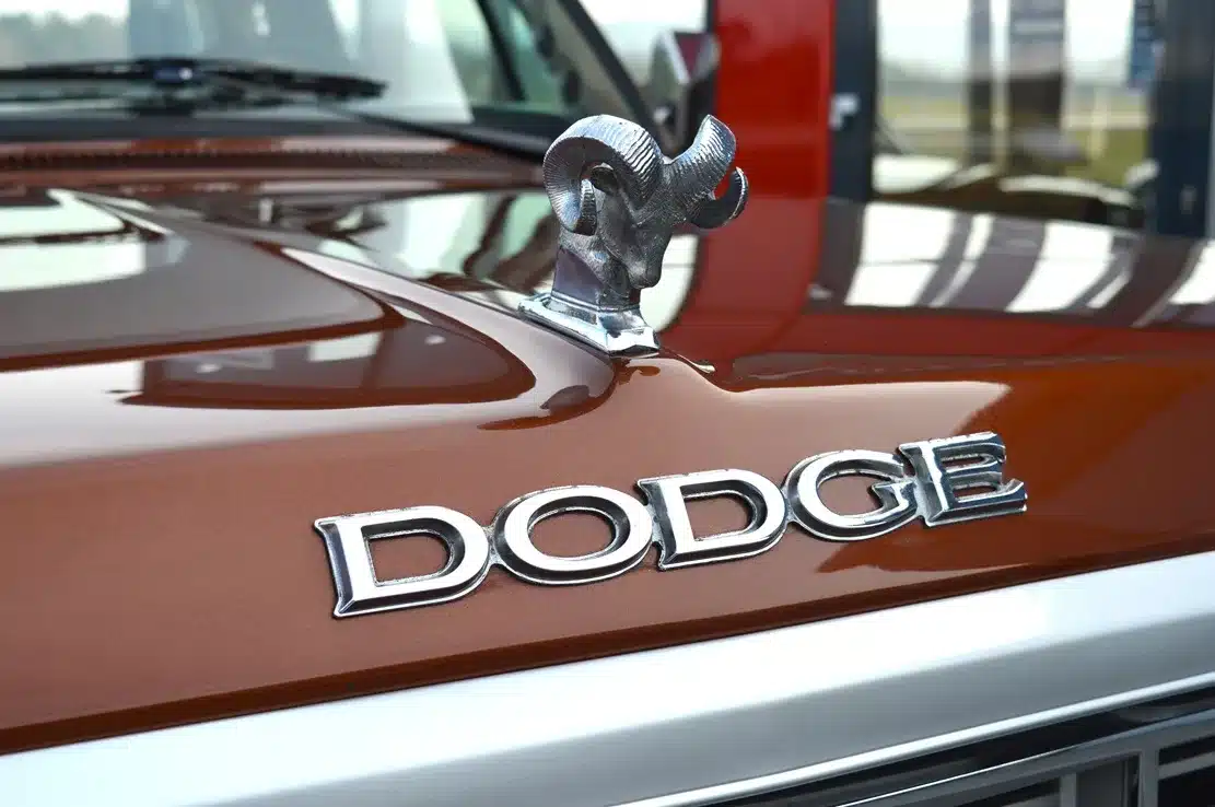 Nahaufnahme der Motorhaube eines Dodge D150 Ram mit Ram-Kühlerfigur und Dodge-Logo, Western Brown Metallic Lackierung.