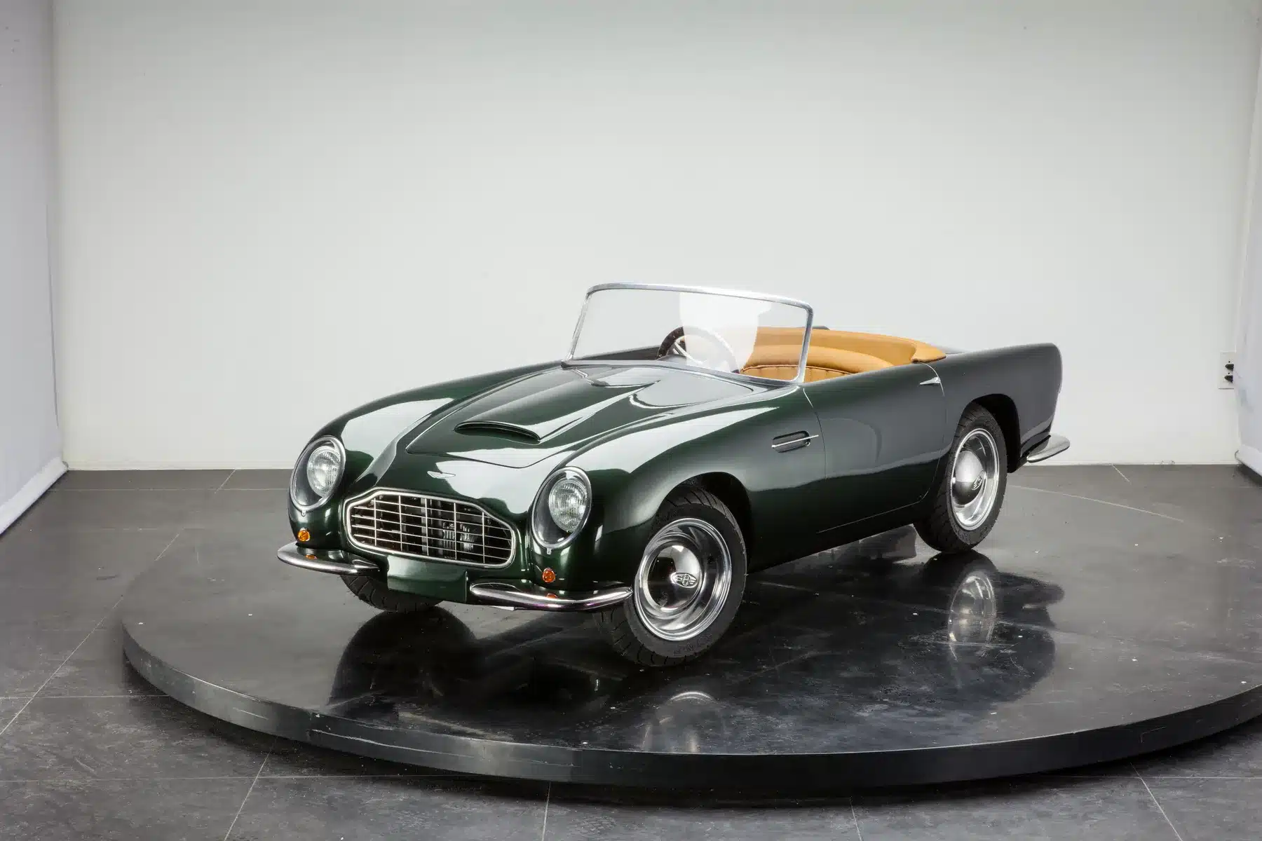 Dunkelgrüner Mini-Gran-Turismo GB Spirit mit beigem Innenraum auf schwarzer Präsentationsplattform, Vorderansicht