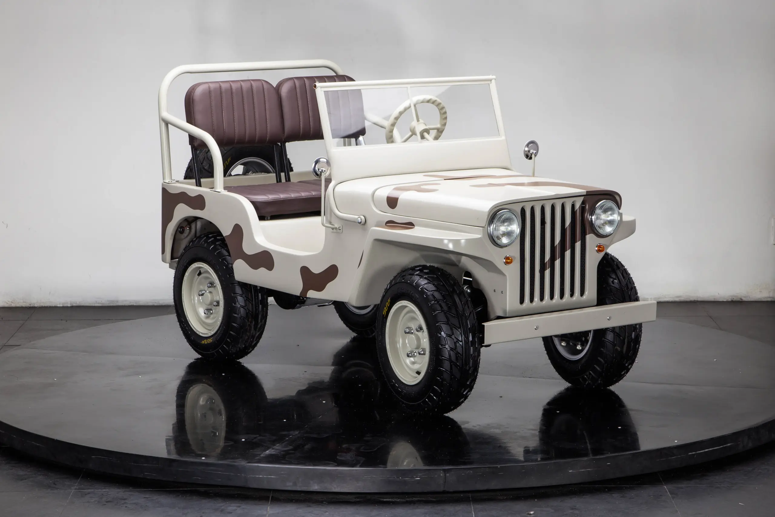 Miniatur-Army-Jeep J-ARMY für Kinder mit Militärlackierung, erhöhtem Sitz und grobstolligen Reifen auf einem Podest