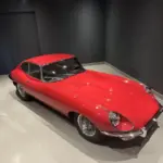 Roter Jaguar E-Type Coupé Serie I in einem Ausstellungsraum, Sicht von schräg oben.