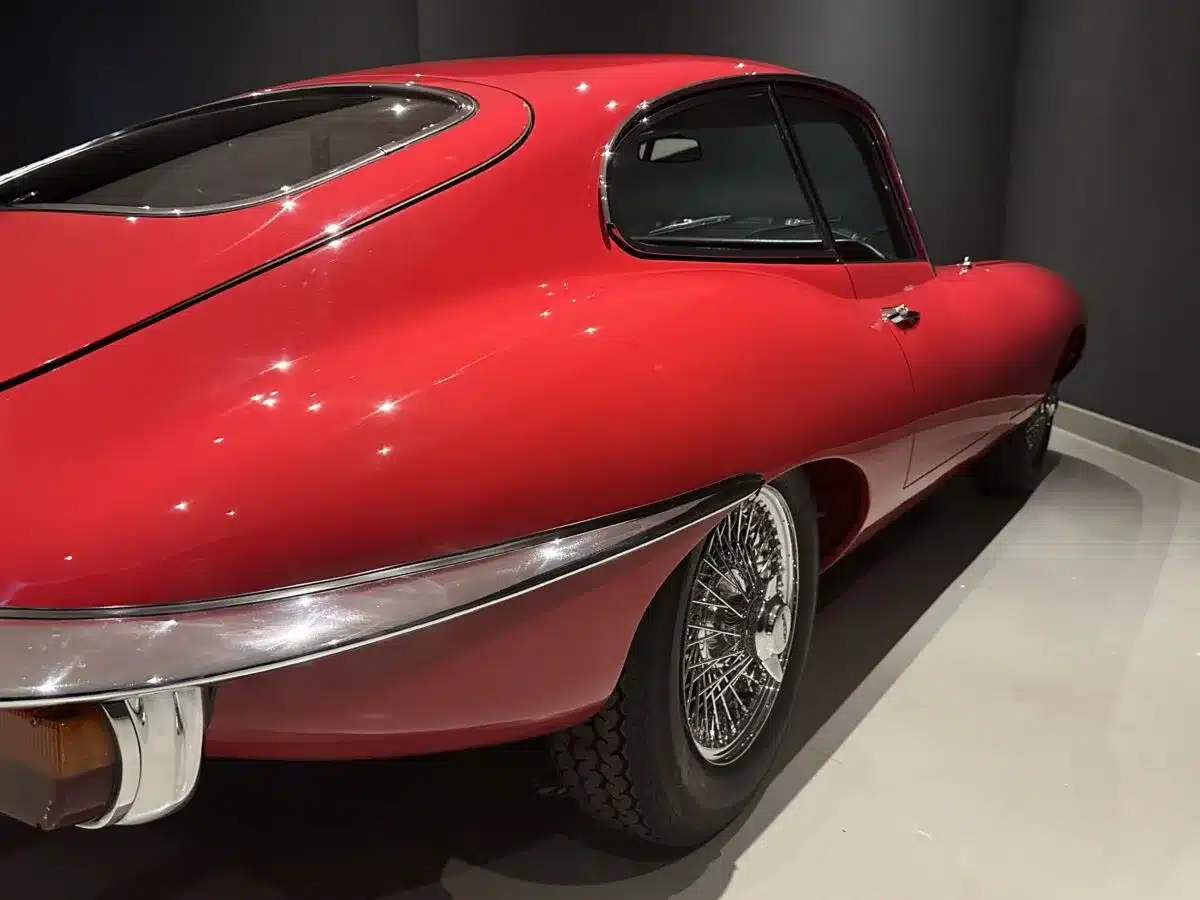 Heck- und Seitenansicht eines roten Jaguar E-Type Coupé, glänzend lackiert, vor dunklem Hintergrund.