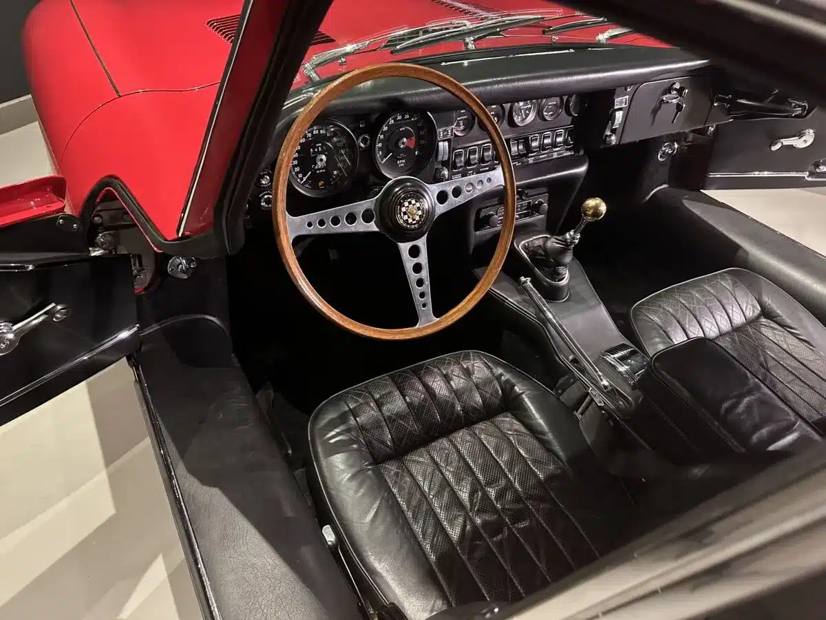 Blick in den Innenraum eines Jaguar E-Type mit Holzlenkrad, Schalthebel und klassischen Rundinstrumenten.