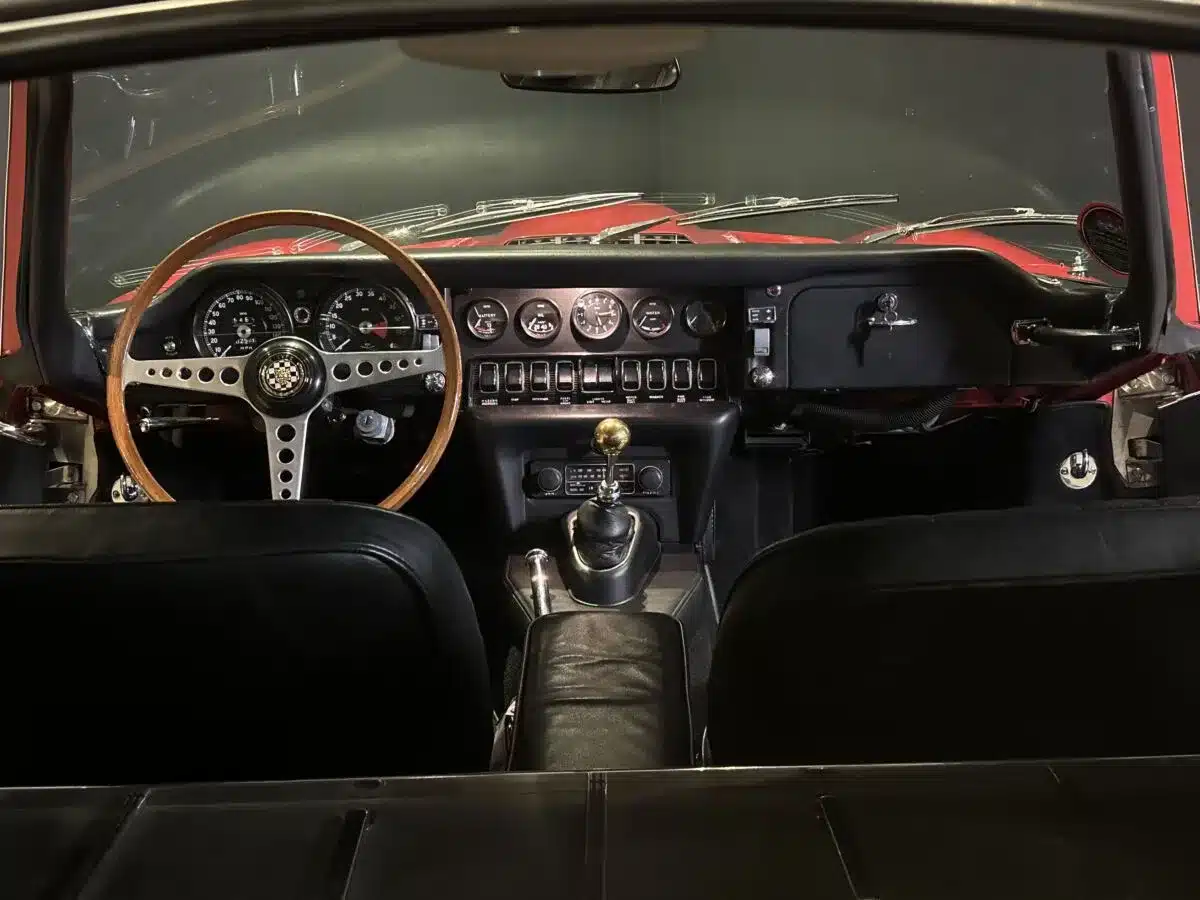 Blick auf das Armaturenbrett und das Lenkrad eines Jaguar E-Type von den Rücksitzen aus gesehen.