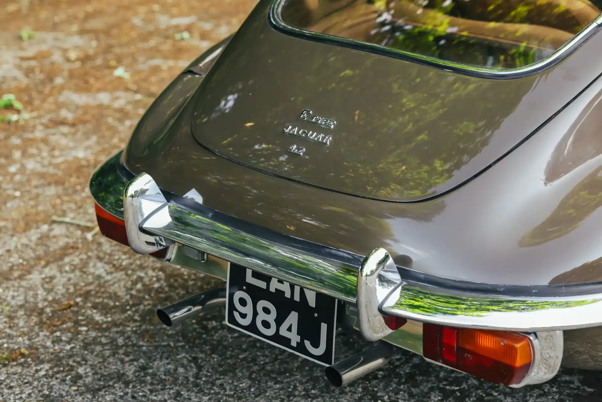 Heck des Jaguar E-Type Series 2 2+2 Coupé 1970 in Sable mit Chromstoßfänger und Typenschild, fotografiert im Freien.