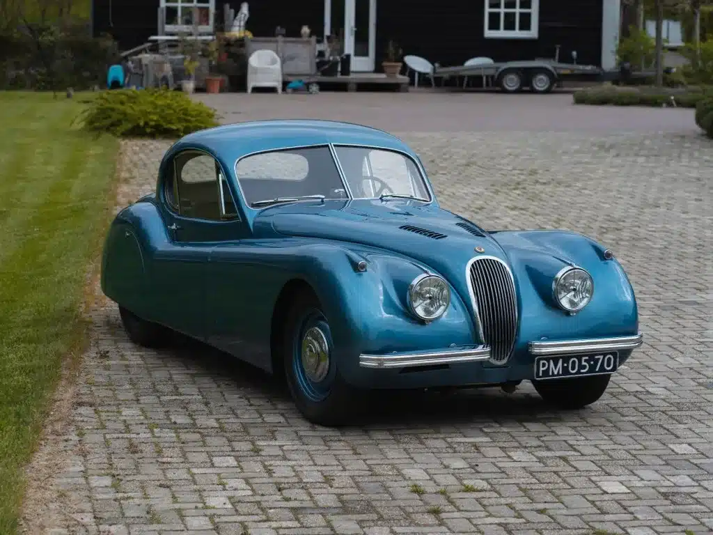 Vollrestaurierter blauer Jaguar XK 120 Fixed Head Coupé Baujahr 1951 auf einer Einfahrt vor einem Haus.