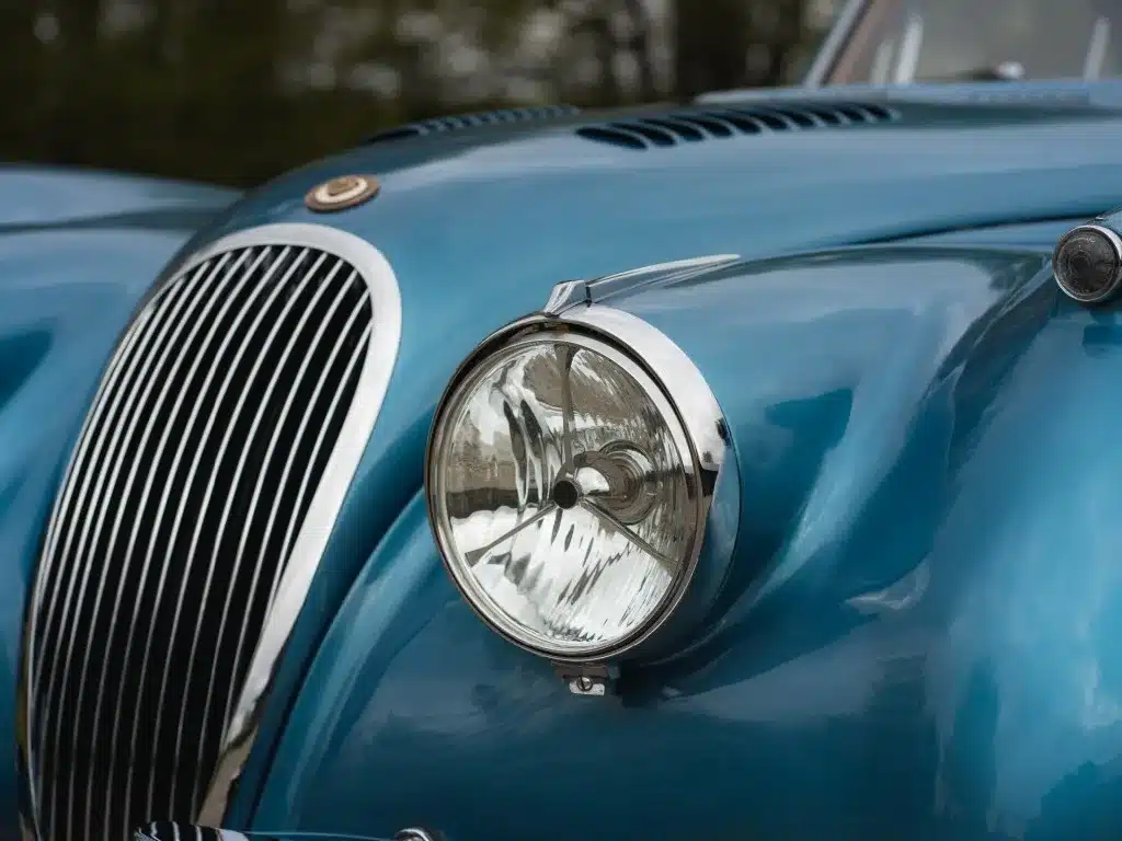 Detailaufnahme des Kühlergrills und Frontscheinwerfers eines blauen Jaguar XK 120 FHC Baujahr 1951