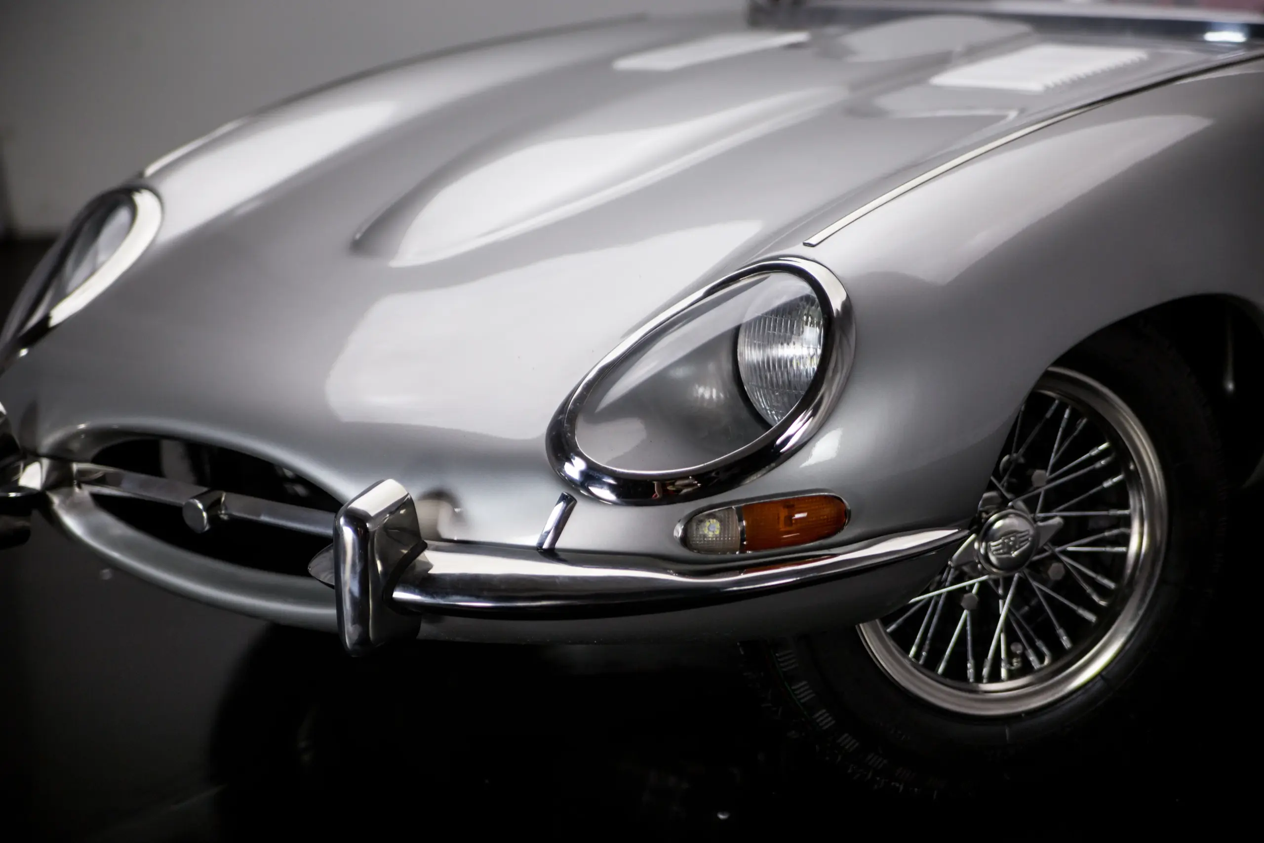 Frontansicht eines silbernen klassischen Sportwagens mit sichtbarem Frontscheinwerfer und Drahtspeichenrad