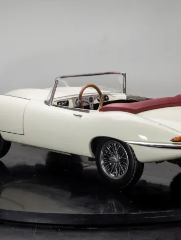 Mini-Sportwagen Junior Series 1 mit weißer Karosserie, rotem Verdeck und filigranen Speichenrädern, fotografiert in einem Studio von schräg hinten.