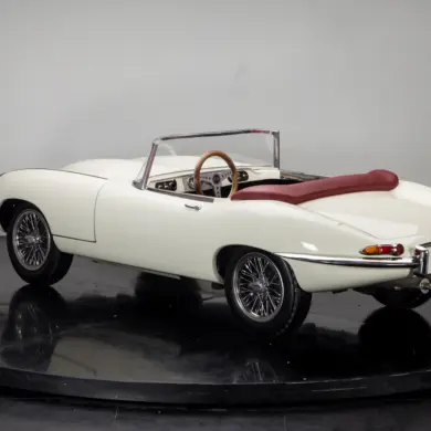 Mini-Sportwagen Junior Series 1 mit weißer Karosserie, rotem Verdeck und filigranen Speichenrädern, fotografiert in einem Studio von schräg hinten.