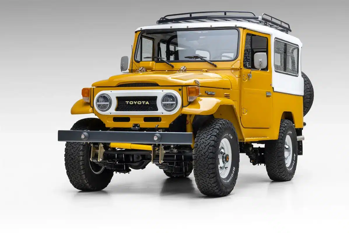 Vorderansicht eines restaurierten, gelben Toyota Land Cruiser mit weißem Dach auf hellem Hintergrund.