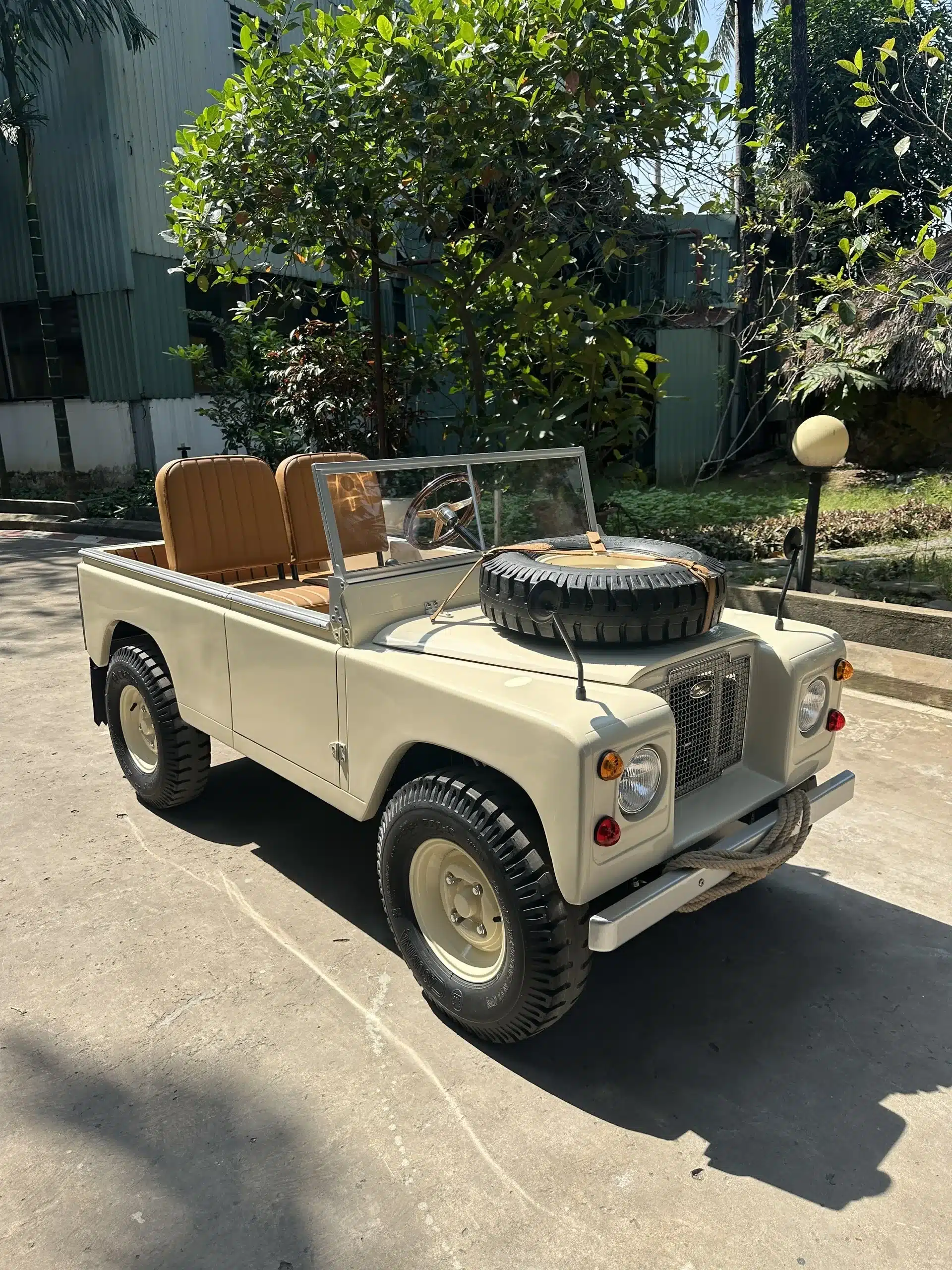 Land Junior Kinderfahrzeug, cremefarben, im Freien geparkt, klassisches Offroad-Design, zwei Sitze, Ersatzrad auf der Motorhaube.