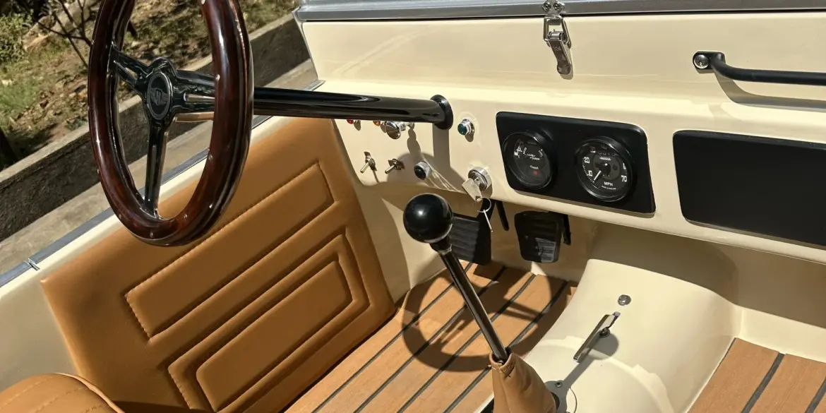 Innenansicht des Land Junior mit Lenkrad, Schalthebel, Pedalen und beigen Ledersitzen in Detailaufnahme.