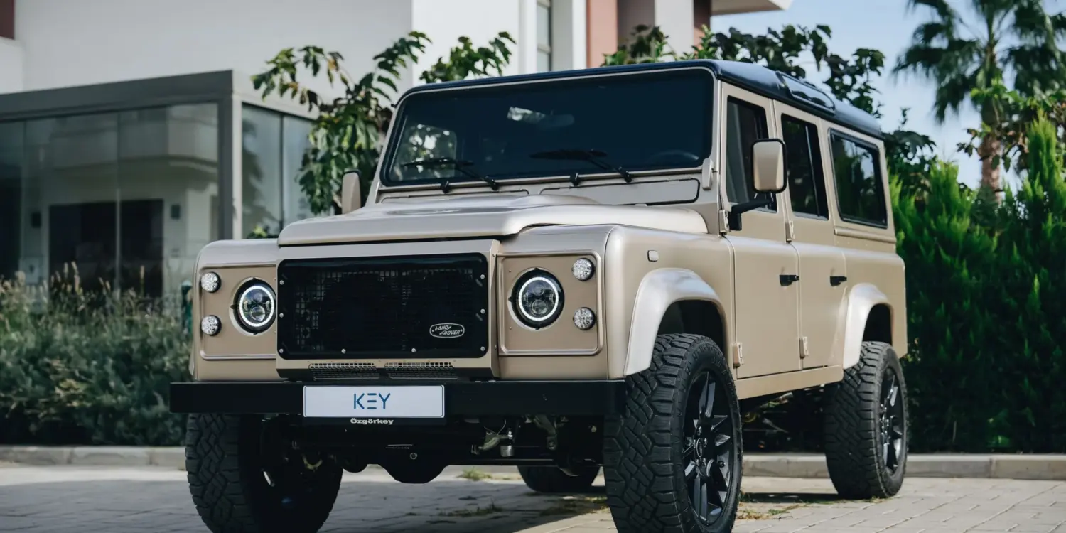 Land Rover Defender 110 V8, Baujahr 1991, beige, vor einem modernen Gebäude geparkt.