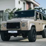 Land Rover Defender 110 V8, Baujahr 1991, beige, vor einem modernen Gebäude geparkt.