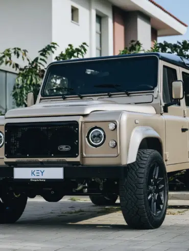 Land Rover Defender 110 V8, Baujahr 1991, beige, vor einem modernen Gebäude geparkt.