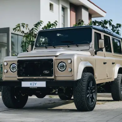 Land Rover Defender 110 V8, Baujahr 1991, beige, vor einem modernen Gebäude geparkt.