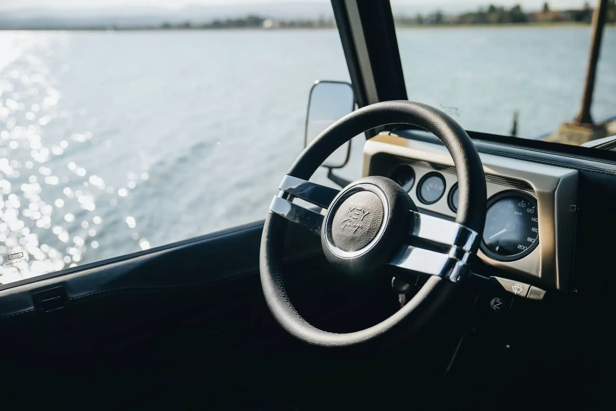 Cockpit und Lenkrad eines Land Rover Defender 110 (1991) mit Blick aufs Wasser durch das Seitenfenster.