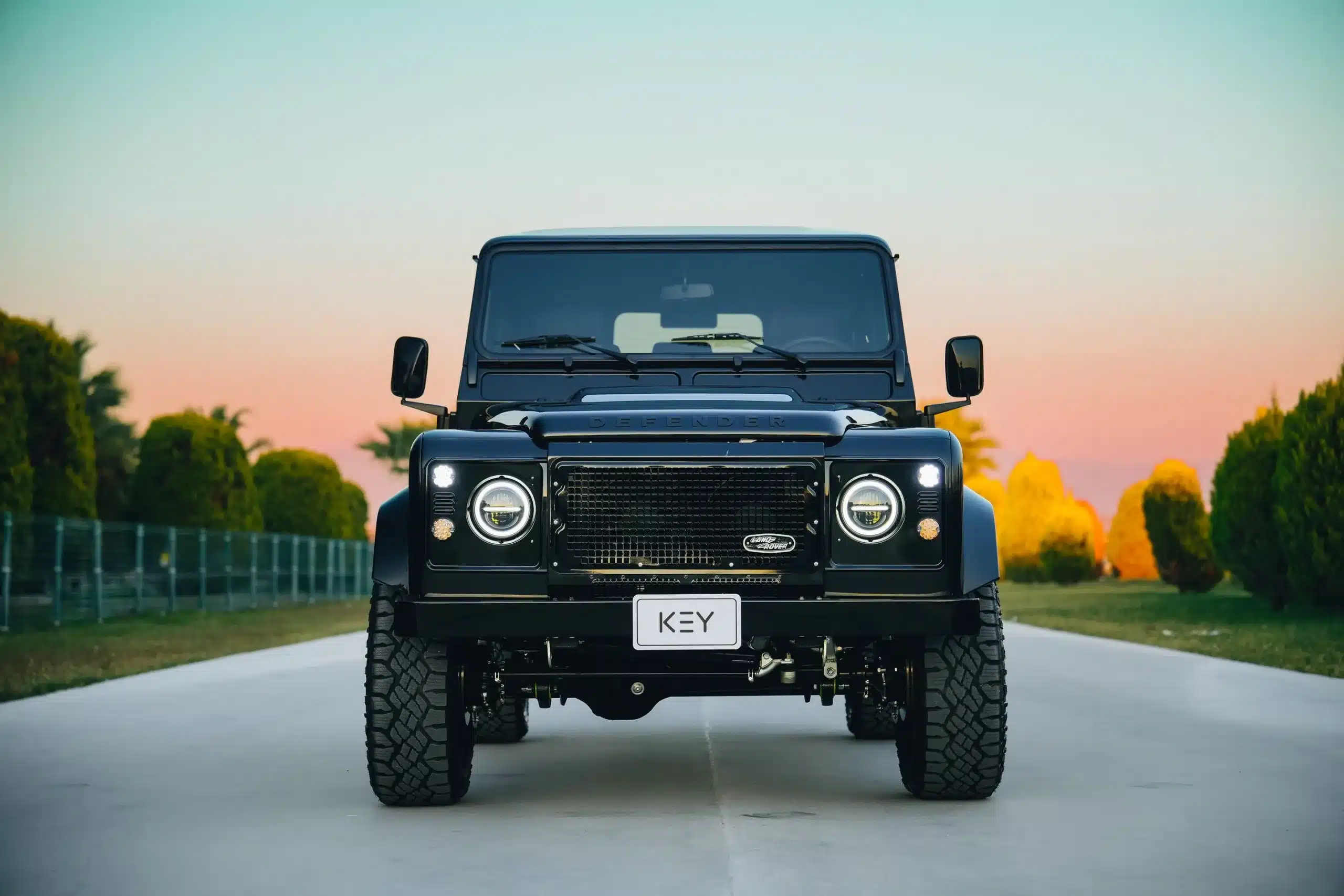Schwarzer Land Rover Defender 110 von vorn auf einer Allee im Sonnenuntergang