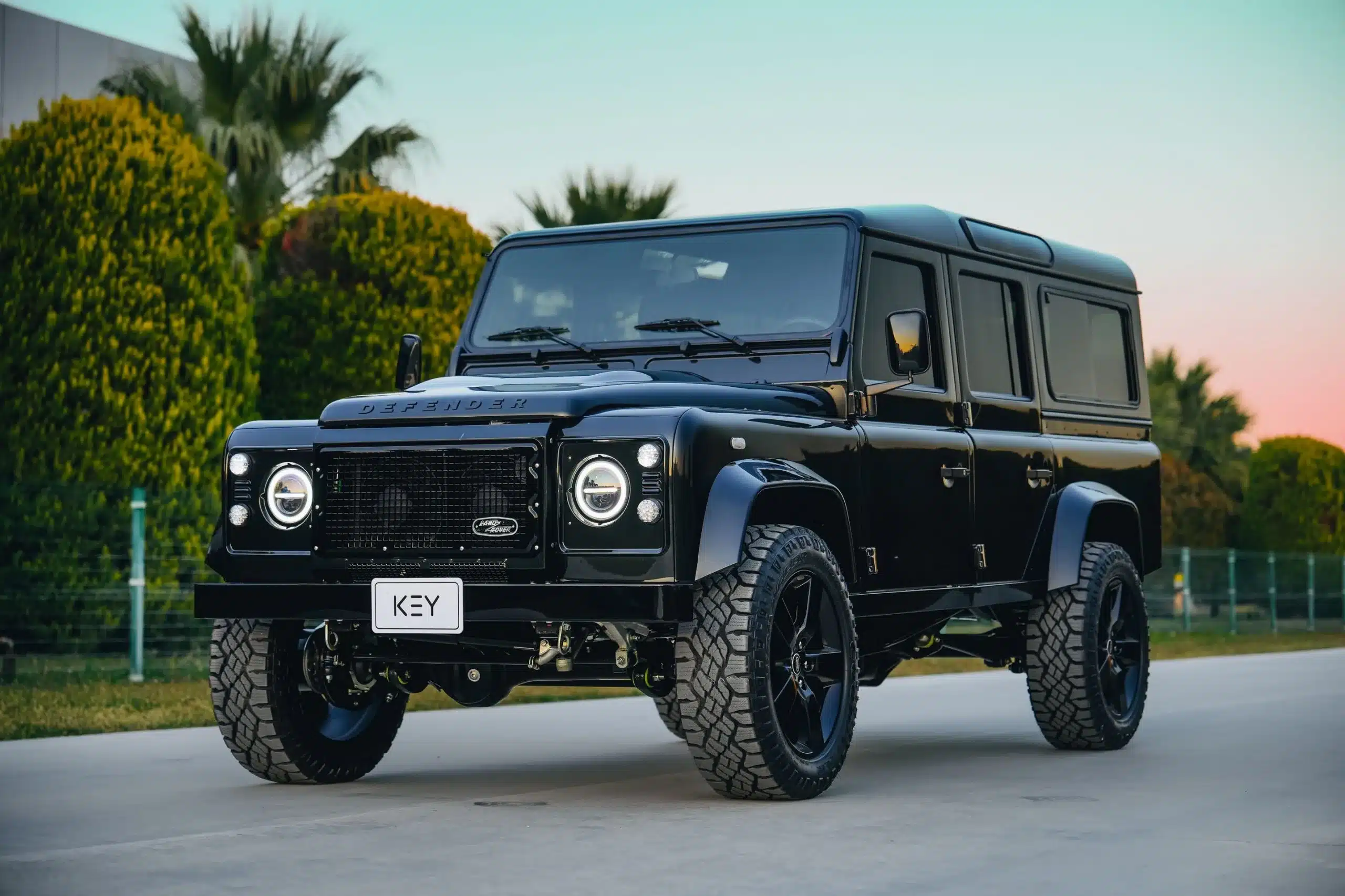 Schwarzer Land Rover Defender 110 mit modernen LED-Scheinwerfern und 20-Zoll-Rädern, fotografiert im Stand auf einer Straße.