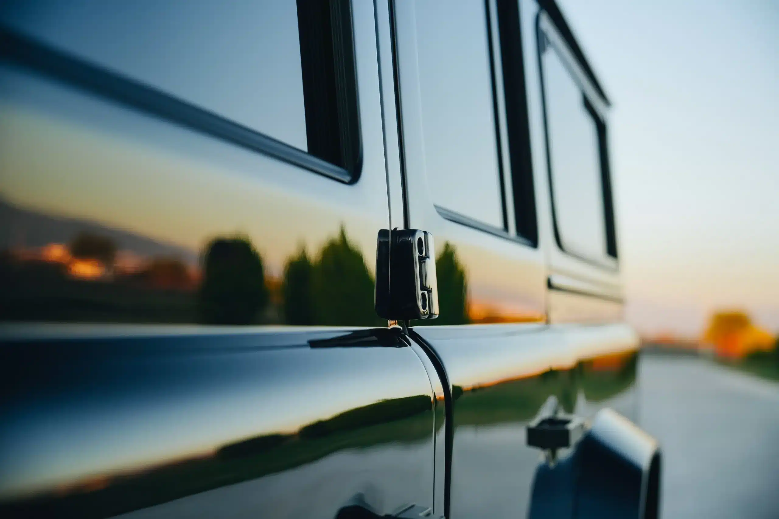 Detailaufnahme der seitlichen Karosserie eines schwarzen Land Rover Defender 110, spiegelnde Oberfläche bei Sonnenuntergang.