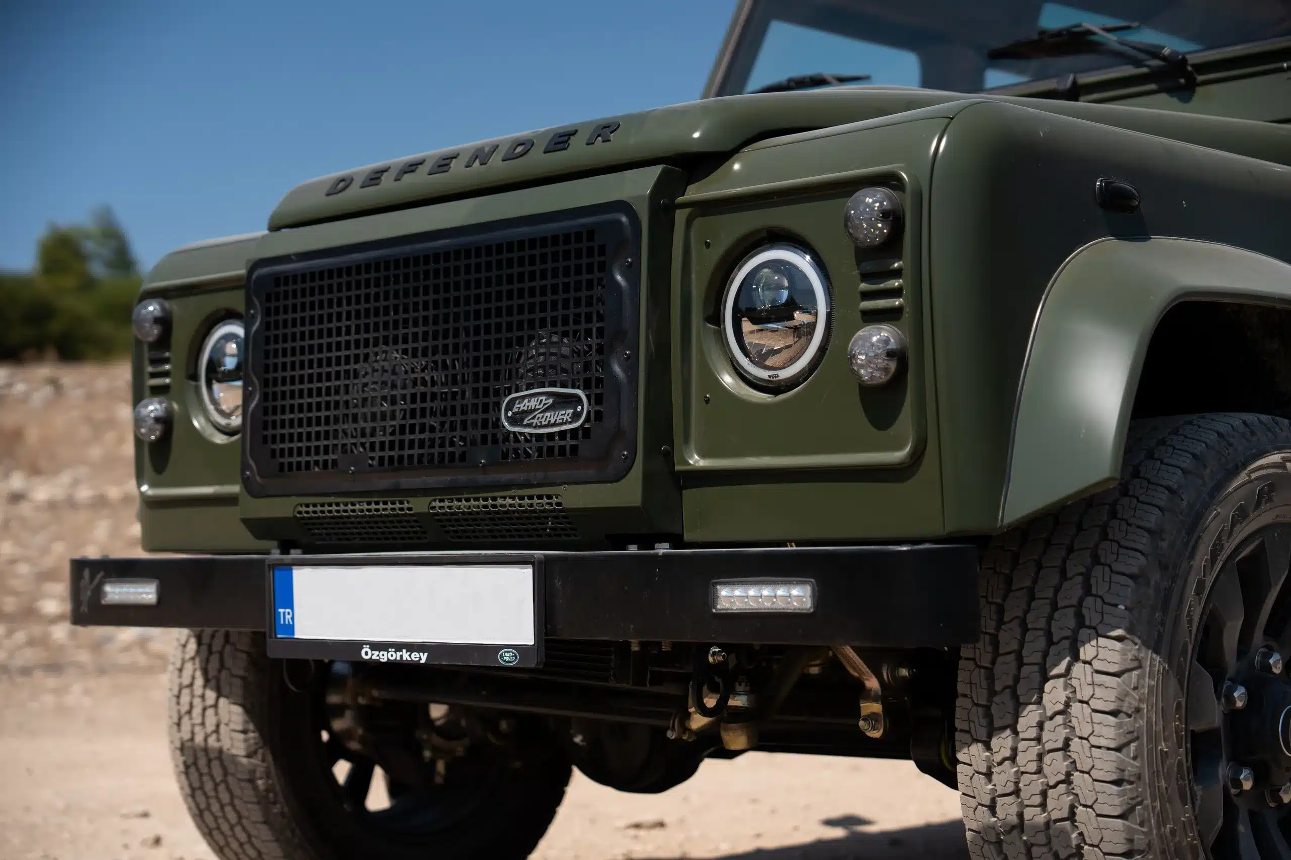 Frontpartie eines olivgrünen Land Rover Defender 110 mit LED-Leuchten und charakteristischem Kühlergrill.