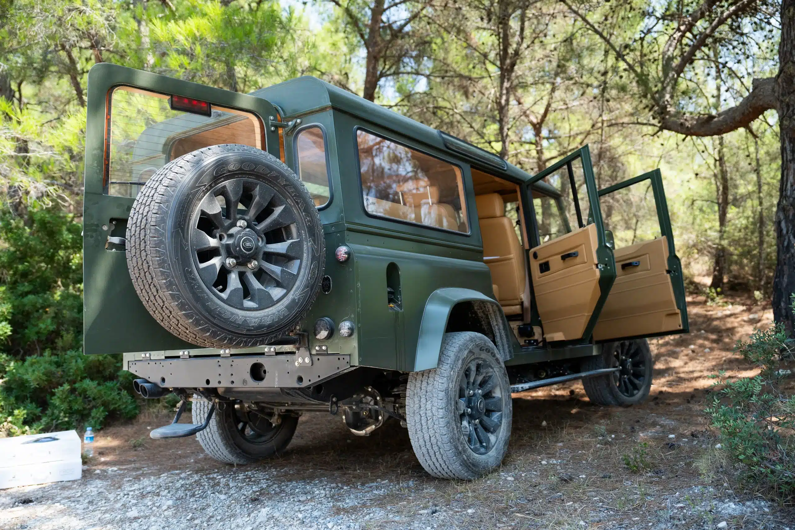 Land Rover Defender 110, Baujahr 1999, in Olivgrün mit geöffneten Türen und Reserverad, steht im Wald