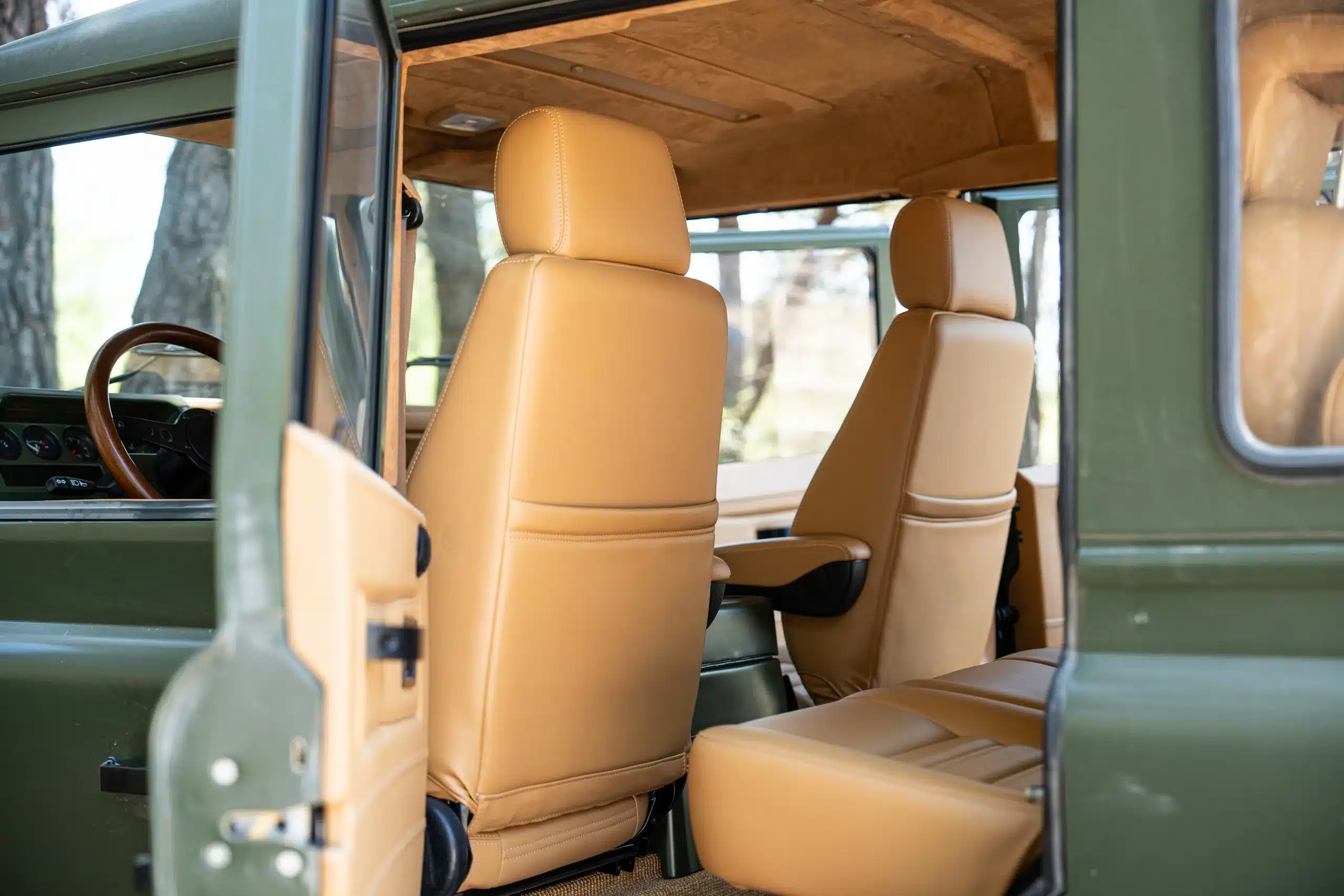 Blick in den Innenraum eines olivgrünen Land Rover Defender 110 von 1999 mit beigen Ledersitzen und Holzdetails