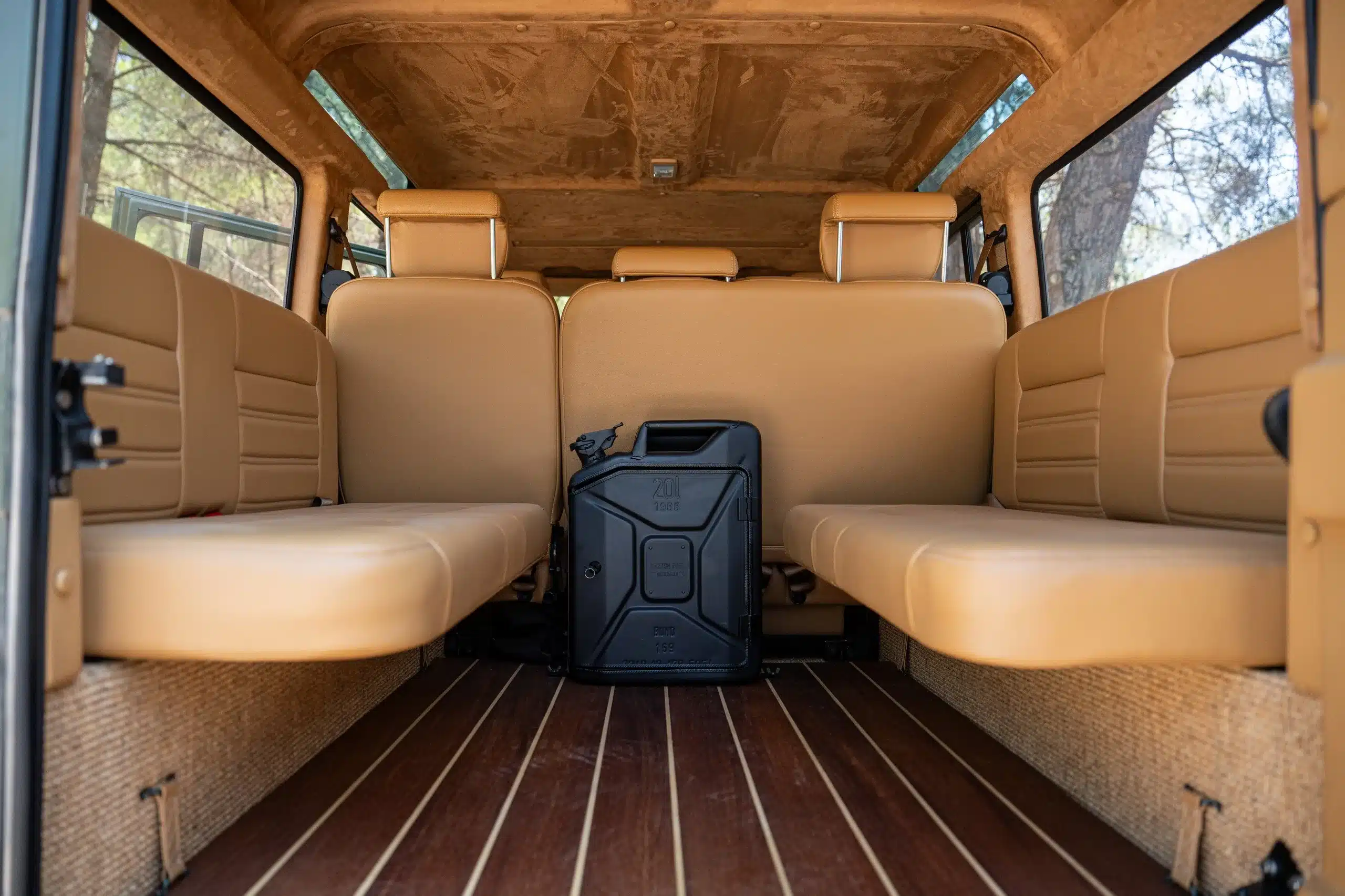 Innenansicht Land Rover Defender 110 (1999) mit Holzboden, beigen Ledersitzen und Danish Fuel Bar Cabinet.