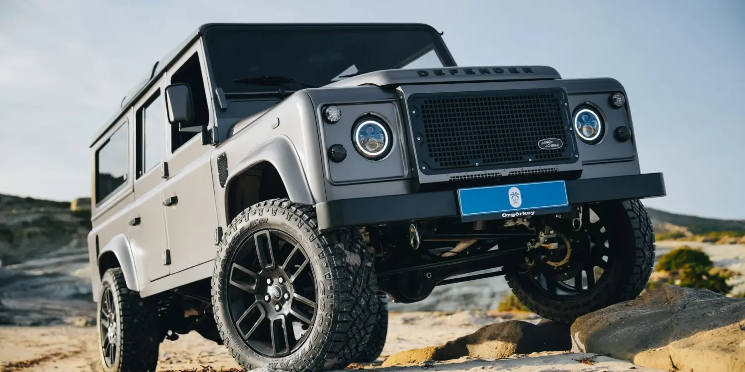 Land Rover Defender 110 in Urban Grey auf sandigem Gelände mit erhöhtem Radstand und Offroad-Bereifung.