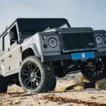 Land Rover Defender 110 in Urban Grey auf sandigem Gelände mit erhöhtem Radstand und Offroad-Bereifung.