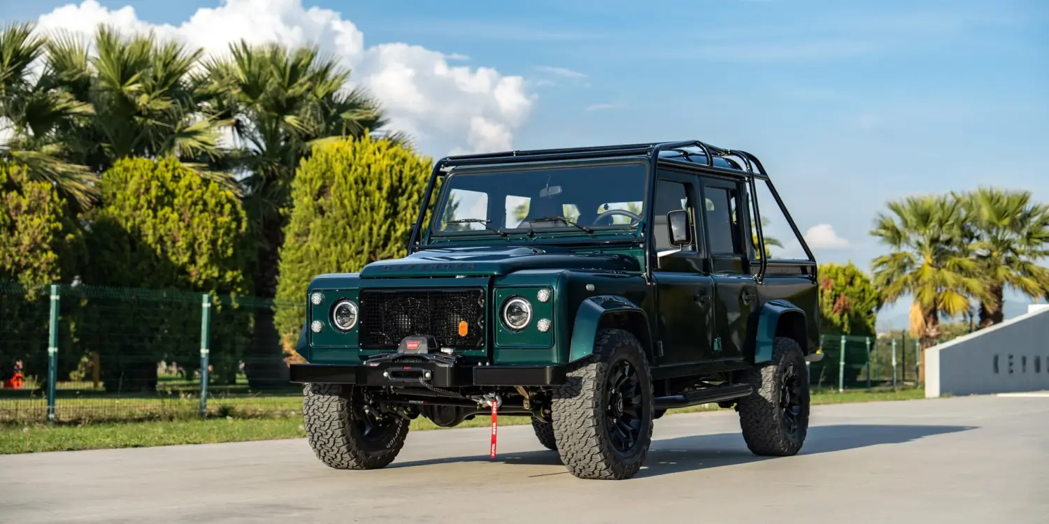 Land Rover Defender 110 von 1994 in Viridian Green, frontal fotografiert, geparkt vor Palmen und blauem Himmel.