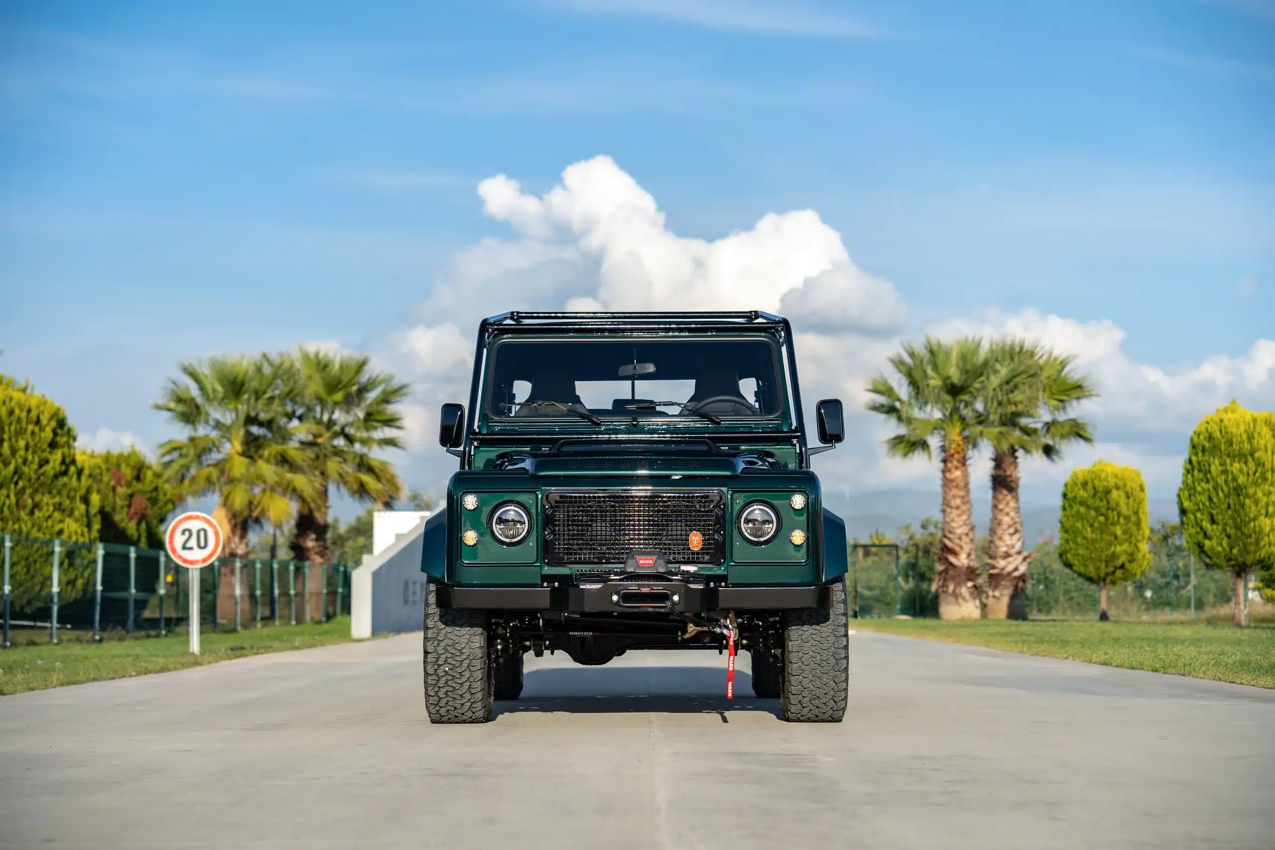 Frontansicht eines Land Rover Defender 110 aus dem Jahr 1994 in Viridian Green auf einer Auffahrt mit Palmen im Hintergrund.