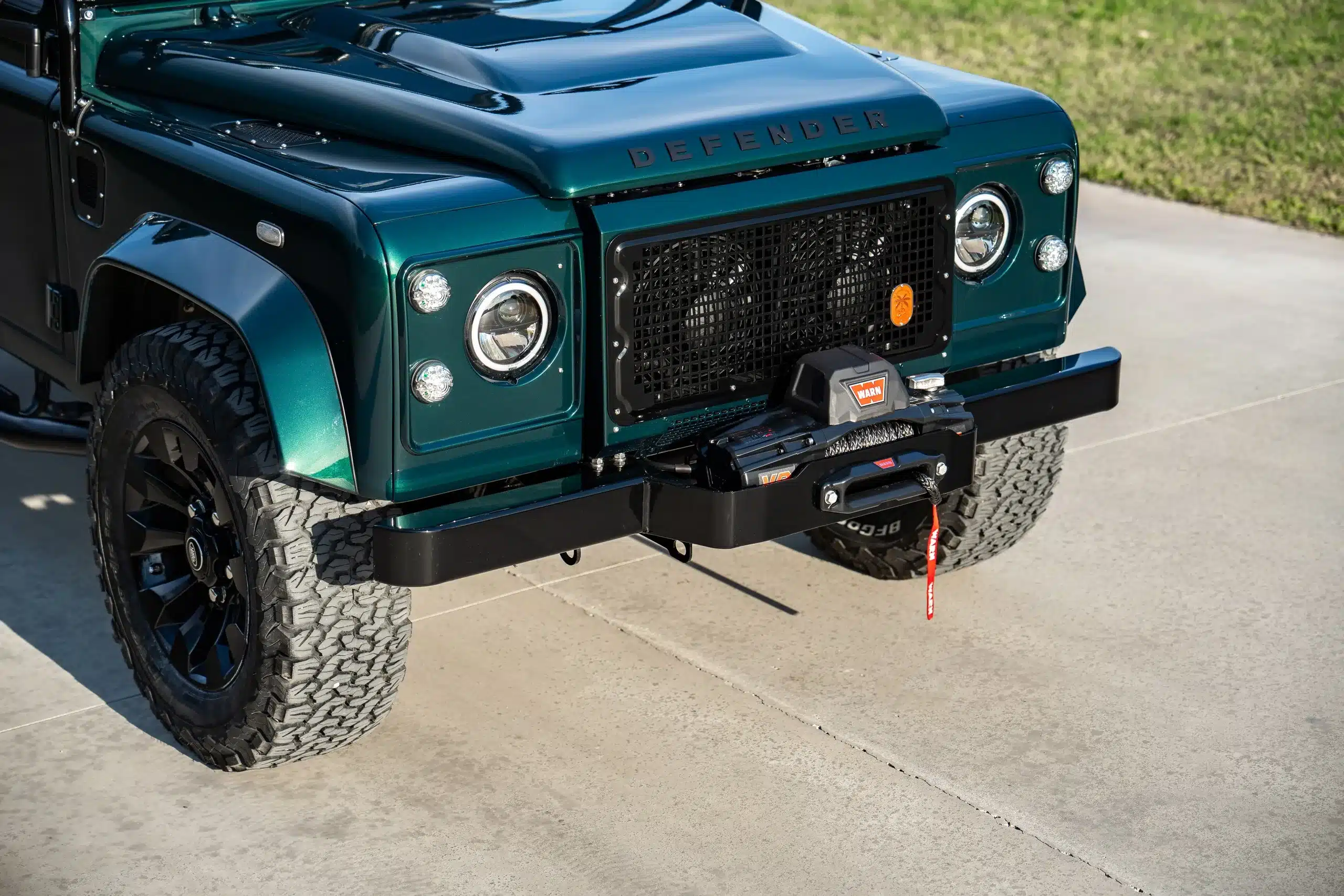 Front des Land Rover Defender 110 in Viridian Green mit markantem Kühlergrill und Seilwinde