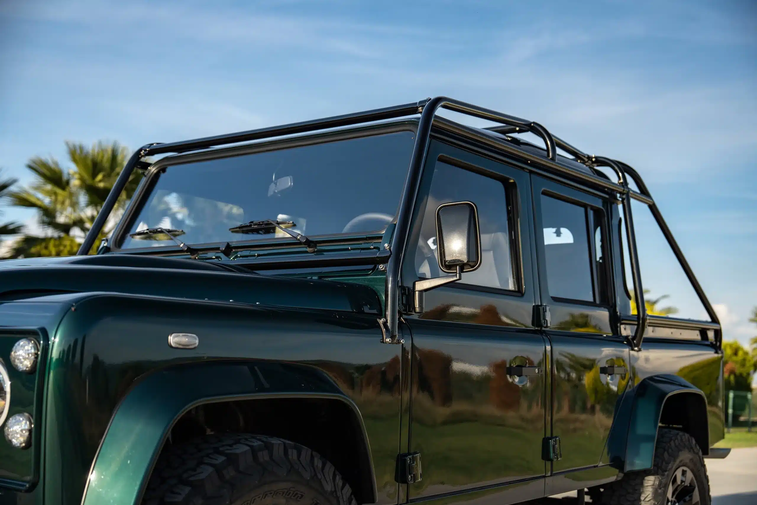 Land Rover Defender 110, Baujahr 1994, in Viridian Green mit Überrollbügel, Nahaufnahme der Front und Kabine bei Tageslicht.