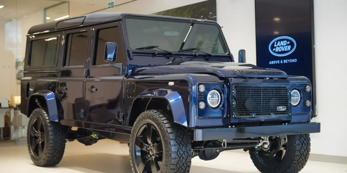 Land Rover Defender 110 300 TDI von 1999 in Tanzanite Blue, modernisiert mit LED-Leuchten und großen 20-Zoll-Rädern, ausgestellt in einem Showroom.