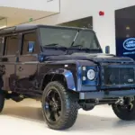 Land Rover Defender 110 300 TDI von 1999 in Tanzanite Blue, modernisiert mit LED-Leuchten und großen 20-Zoll-Rädern, ausgestellt in einem Showroom.