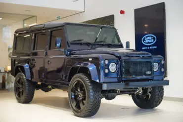 Land Rover Defender 110 300 TDI von 1999 in Tanzanite Blue, modernisiert mit LED-Leuchten und großen 20-Zoll-Rädern, ausgestellt in einem Showroom.